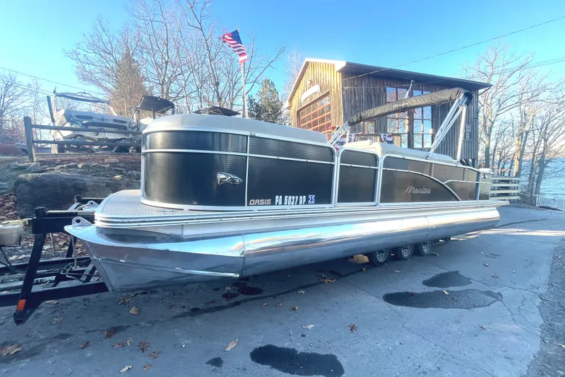 Slide: The Image of 2015 Manitou 25 Oasis SR pontoon boat on trailer near rustic building. - 1