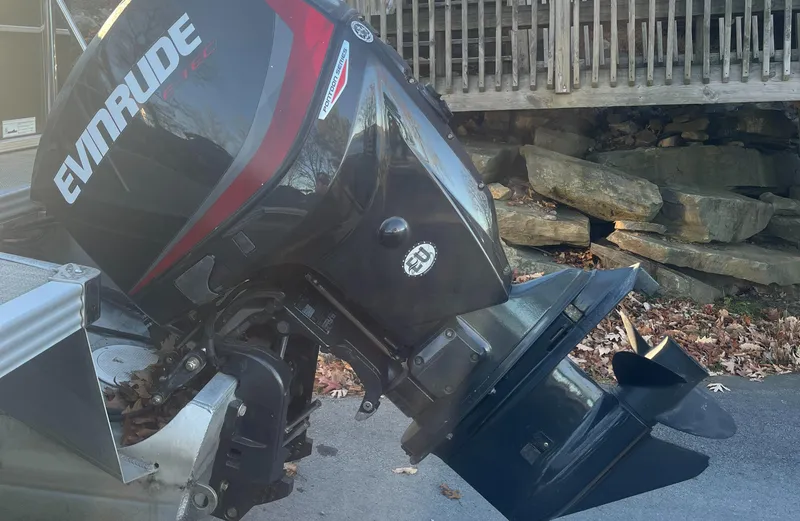 Slide: The Image of Evinrude outboard motor on a 2015 Manitou 25 Oasis SR boat, parked near stone wall. - 10