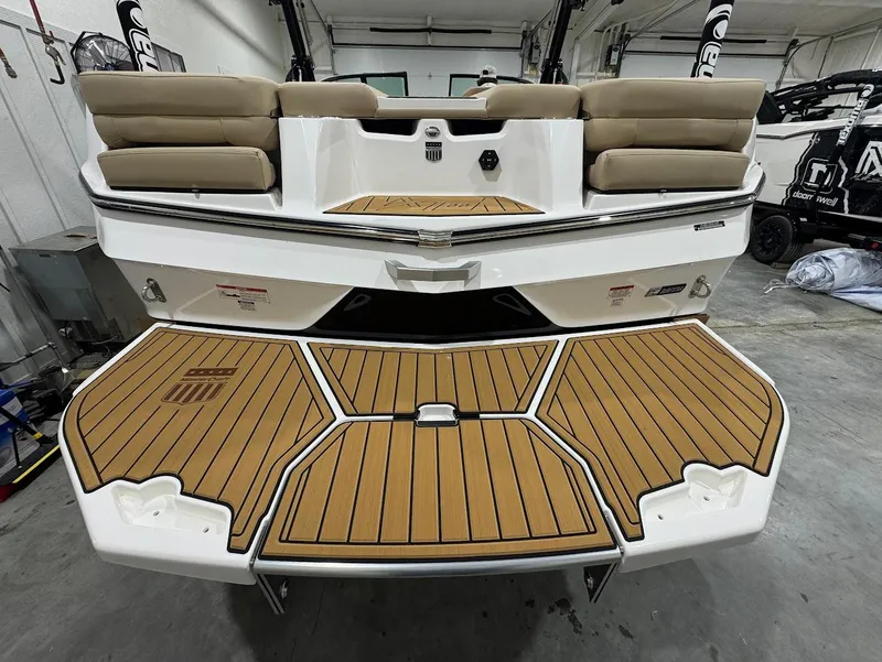 Slide: The Image of 2025 MasterCraft XT22 boat with teak deck, beige seating, and sleek design in a showroom. - 2
