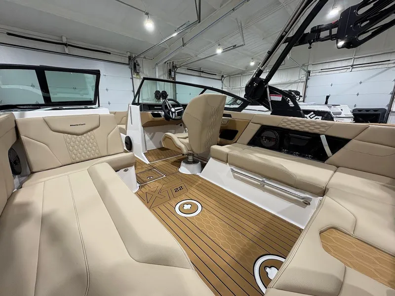 Slide: The Image of 2025 MasterCraft XT22 boat interior with beige seating and wood flooring in a showroom. - 9