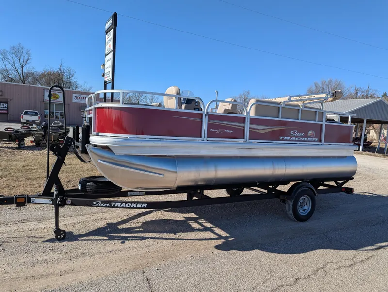 The Image of 2025 Sun Tracker Bass Buggy 18 DLX pontoon boat on trailer, parked outdoors. - 1