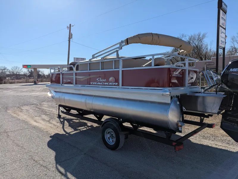 Slide: The Image of 2025 Sun Tracker Bass Buggy 18 DLX pontoon boat on trailer, parked outdoors. - 3