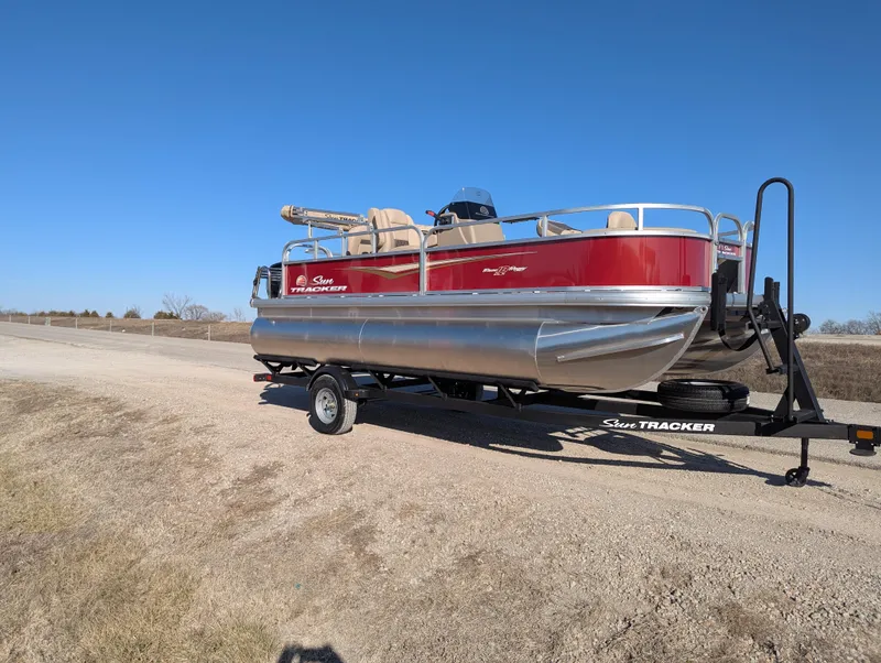 Slide: The Image of 2025 Sun Tracker Bass Buggy 18 DLX pontoon boat on trailer, parked on roadside. - 7
