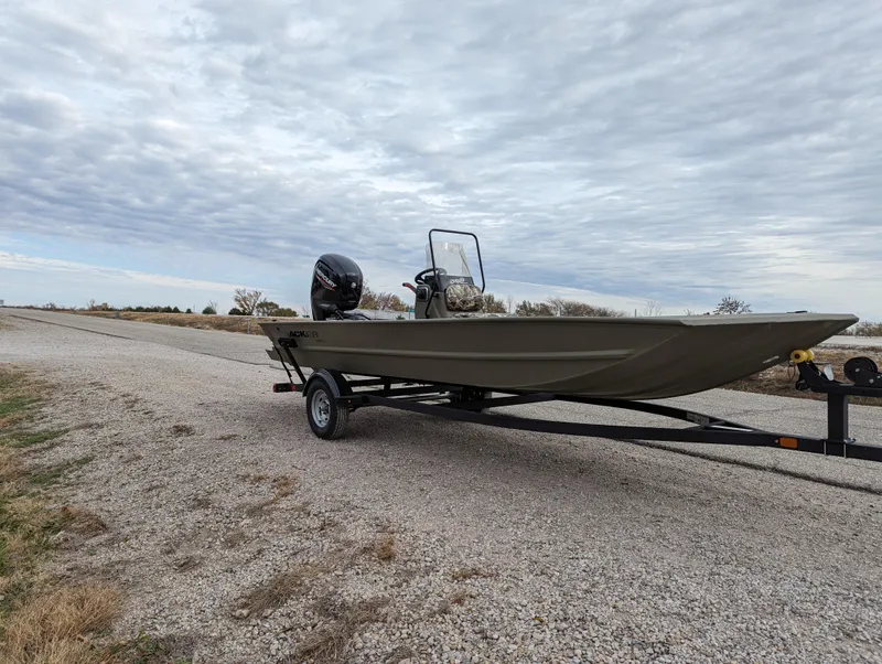 Slide: The Image of 2025 Tracker Grizzly 1860 CC boat on trailer, parked on gravel road under cloudy sky. - 8
