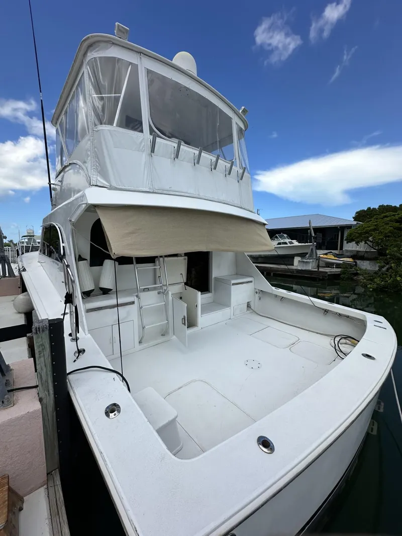 Slide: The Image of 1998 Post 50 Sportfish yacht docked, featuring spacious deck and enclosed flybridge under clear blue sky. - 11