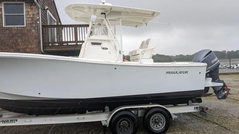 Slide: The Image of 2017 Regulator 23 boat on trailer, parked near a wooden building. - 13