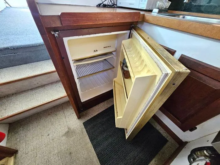 Slide: The Image of 1978 Mainship 34 Sedan interior with open fridge near wooden stairs. - 10