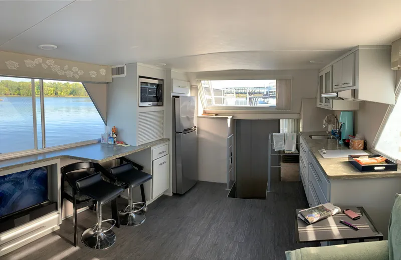 Slide: The Image of 1977 Gibson Standard houseboat interior with modern kitchen, bar stools, and scenic water view. - 2