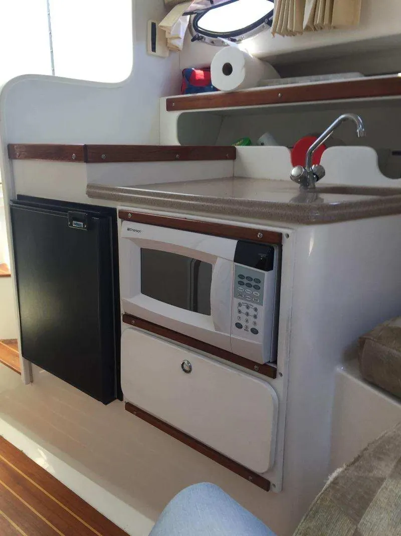 Slide: The Image of 2004 Stamas 310 Express boat interior with kitchenette, featuring a microwave, sink, and mini-fridge. - 7