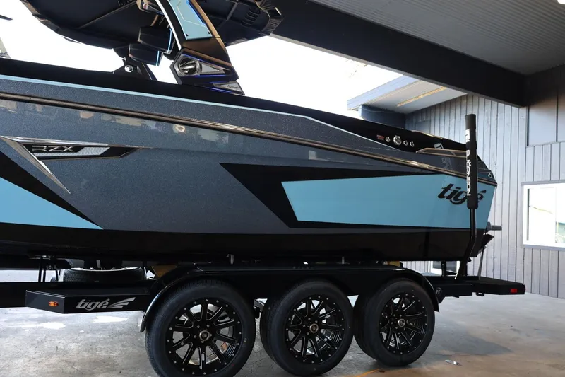 Slide: The Image of 2025 Tigé 24RZX boat on a triple-axle trailer, featuring sleek black and blue design. - 9