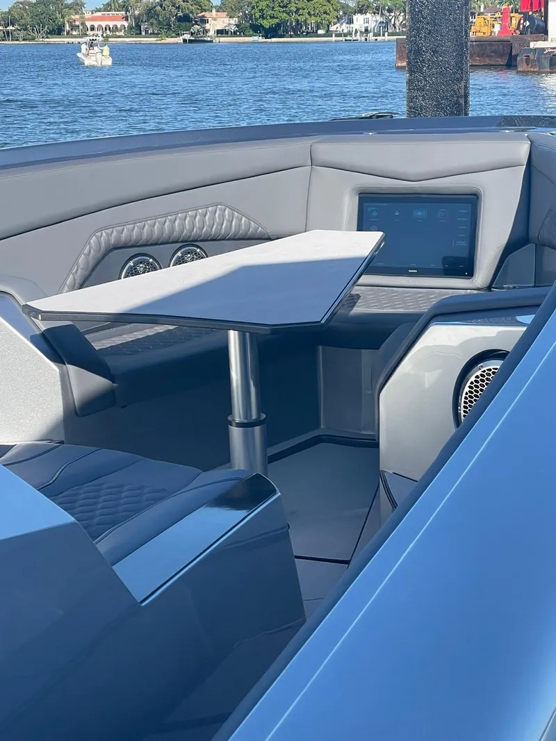 Slide: The Image of 2024 Adrenaline 47 Reaper boat interior with seating and table, docked by the water. - 47