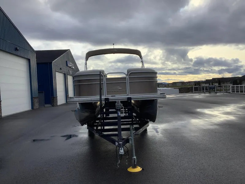 Slide: The Image of 2013 Bennington 2275 pontoon boat on trailer, parked outside marina under cloudy sky. - 3