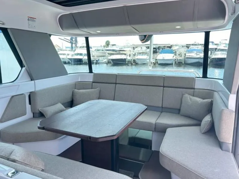 Slide: The Image of 2024 Axopar 45 XC Cross Cabin interior with plush seating and table, overlooking marina. - 22