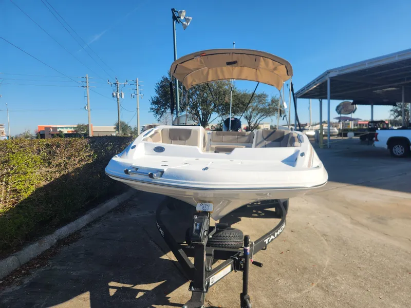 Slide: The Image of 2025 Tahoe 1950 boat with canopy on trailer, parked outdoors under clear blue sky. - 2