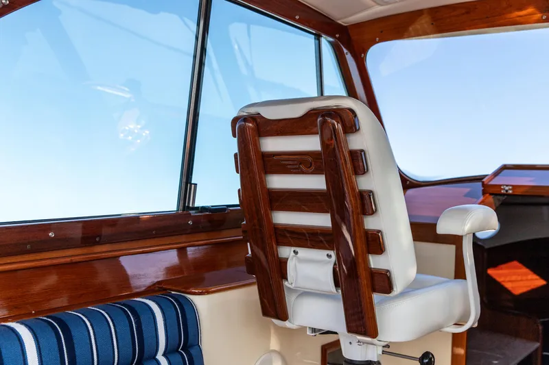 Slide: The Image of 2022 Hinckley Picnic Boat 34 S interior with wooden helm seat and blue-striped cushion. - 13