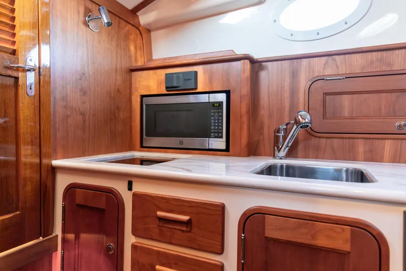 Slide: The Image of 2022 Hinckley Picnic Boat 34 S with blue-striped seating, wooden trim, and scenic water view. - 18