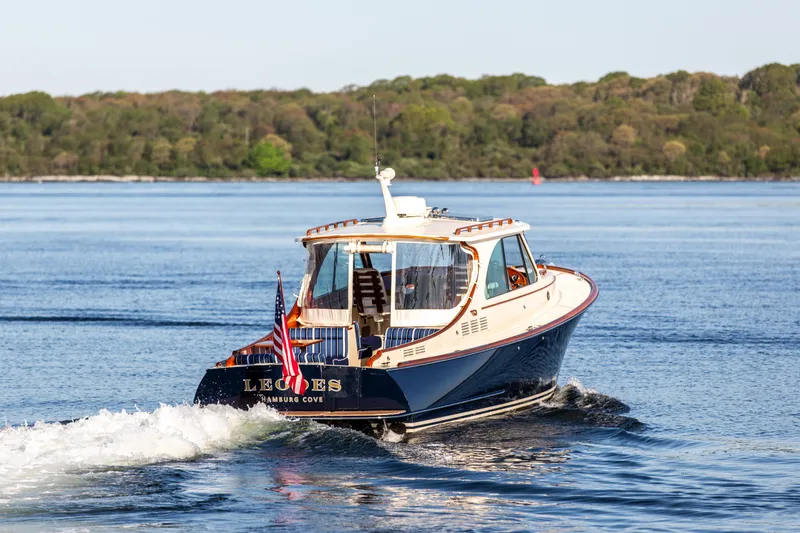 Slide: The Image of 2022 Hinckley Picnic Boat 34 S cruising on a serene lake with lush green shoreline. - 25