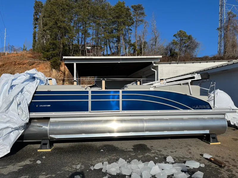 Slide: The Image of 2025 Harris Cruiser 230 pontoon boat in a driveway, partially covered, with trees in the background. - 3