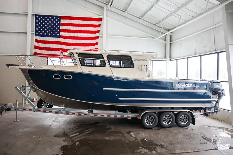 The Image of 2025 Hewescraft 290 Adventure ET HT boat on trailer, indoors, with American flag backdrop. - 0