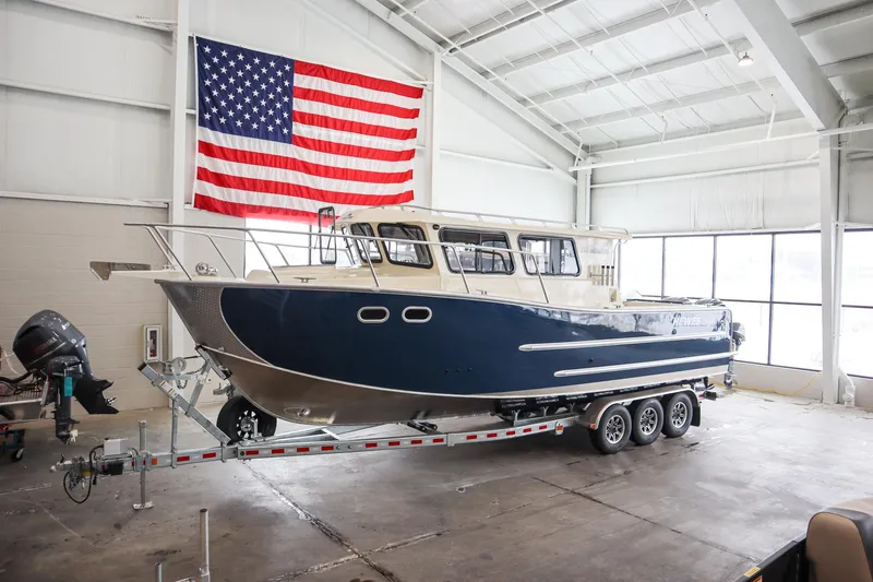 Slide: The Image of 2025 Hewescraft 290 Adventure ET HT boat in a showroom with American flag backdrop. - 3