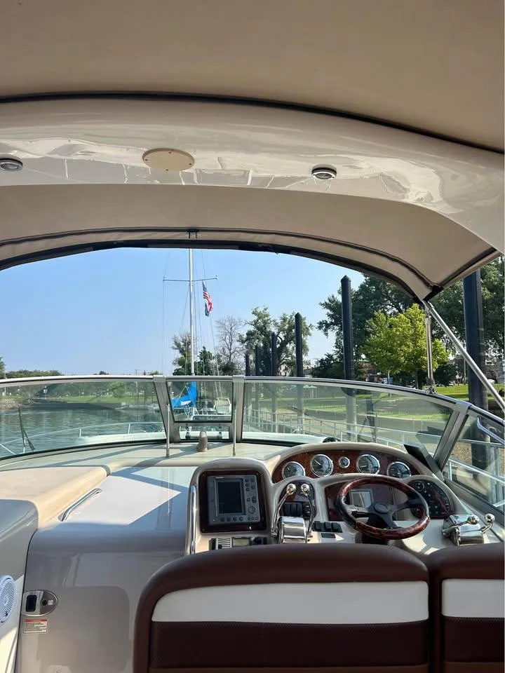 Slide: The Image of 2003 Sea Ray 320 Sundancer cockpit with steering wheel and dashboard, docked near trees. - 7