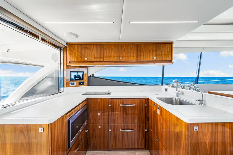 Slide: The Image of Luxurious 2022 Riviera 505 SUV yacht kitchen with ocean view, featuring sleek wood cabinetry and modern appliances. - 34