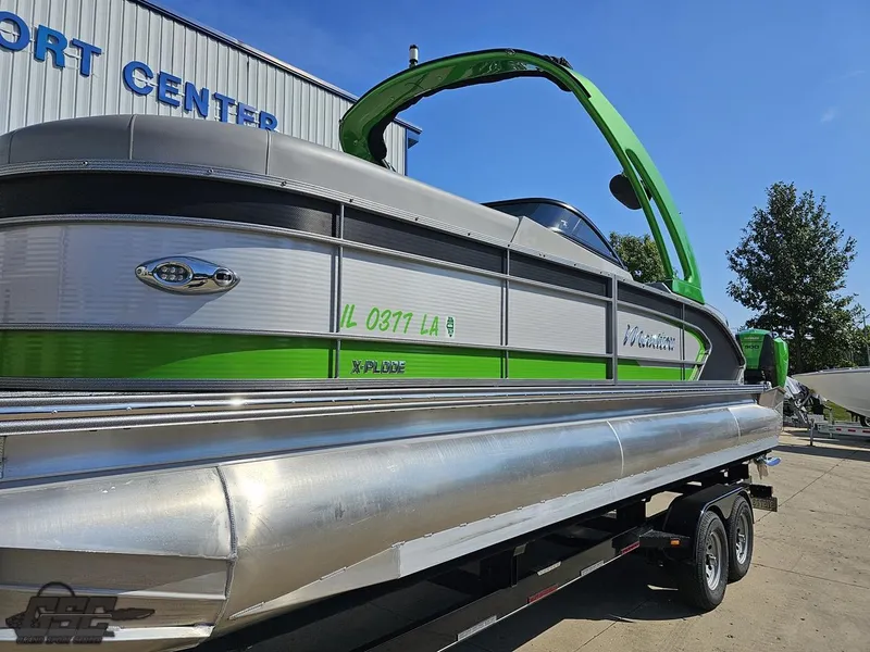 Slide: The Image of 2021 Manitou 25 X-Plode pontoon boat on trailer, green and silver design, parked outside. - 10