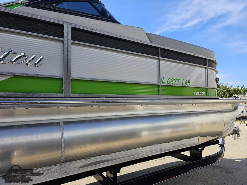 Slide: The Image of 2021 Manitou 25 X-Plode pontoon boat with green accents on a trailer. - 28