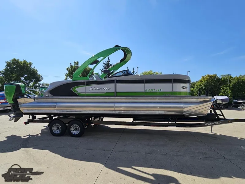 Slide: The Image of 2021 Manitou 25 X-Plode pontoon boat on trailer, green and silver design, sunny day. - 30