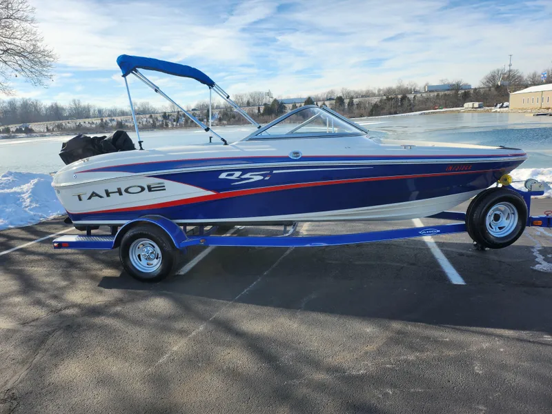 Slide: The Image of 2014 Tahoe Q5i SF boat on trailer by a lake, blue and white design. - 9