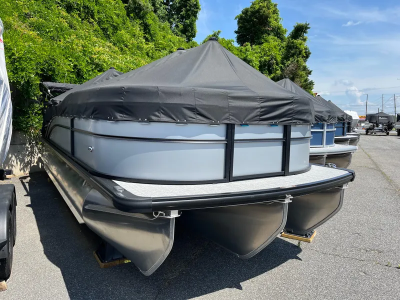 Slide: The Image of 2025 Harris Cruiser 210 pontoon boat with cover, parked outdoors on a sunny day. - 2