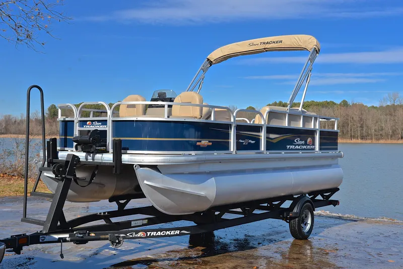 Slide: The Image of 2023 Sun Tracker Bass Buggy 18 DLX pontoon boat on trailer by a lake. - 10