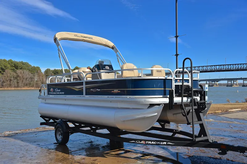 Slide: The Image of 2023 Sun Tracker Bass Buggy 18 DLX pontoon boat on trailer by a lake. - 16