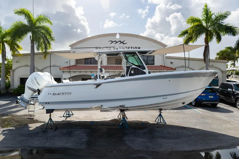 Slide: The Image of 2023 Blackfin 302CC boat displayed outdoors with palm trees and building backdrop. - 1