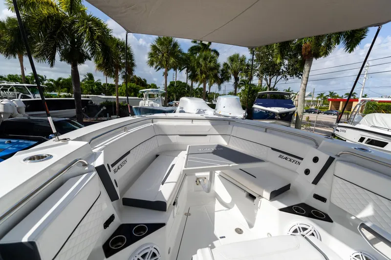 Slide: The Image of 2023 Blackfin 302CC boat interior with seating and table, surrounded by palm trees. - 47