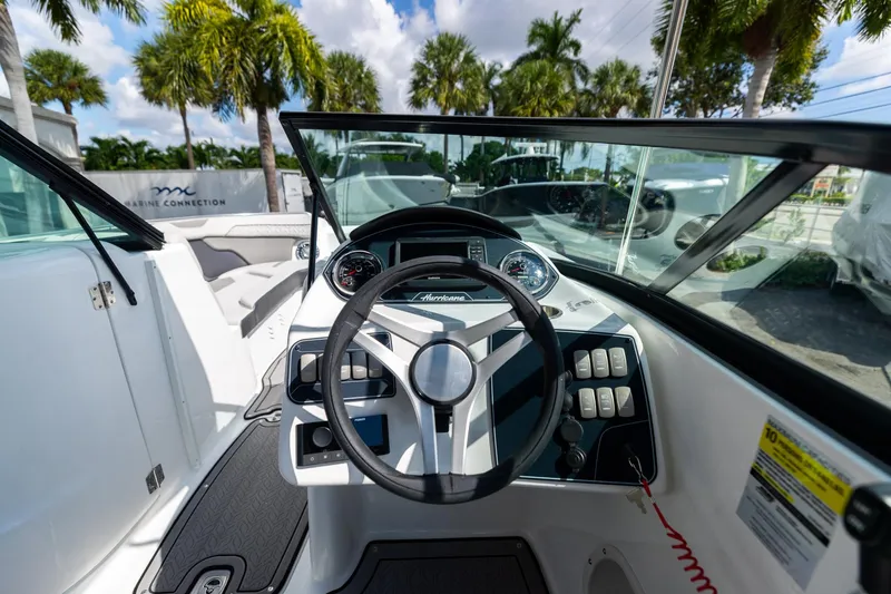 Slide: The Image of 2023 Hurricane SunDeck 2200 OB boat cockpit with steering wheel and controls, surrounded by palm trees. - 16