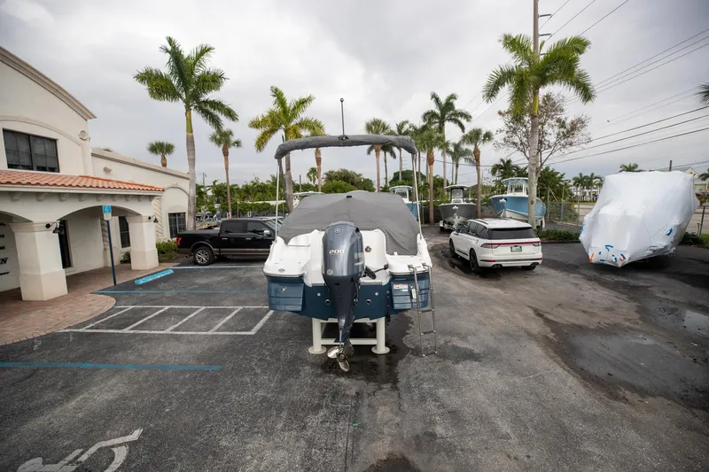 Slide: The Image of 2023 Hurricane SunDeck 2200 OB boat parked outdoors with palm trees and vehicles nearby. - 10
