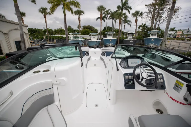 Slide: The Image of 2023 Hurricane SunDeck 2200 OB boat interior with steering wheel and seating, surrounded by palm trees. - 19