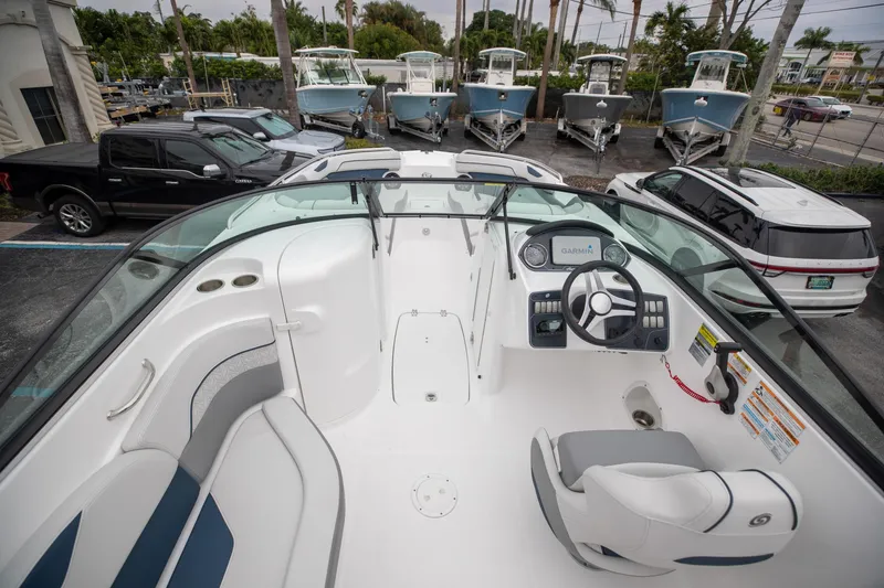 Slide: The Image of 2023 Hurricane SunDeck 2200 OB boat interior with steering wheel and seating, parked near vehicles. - 13