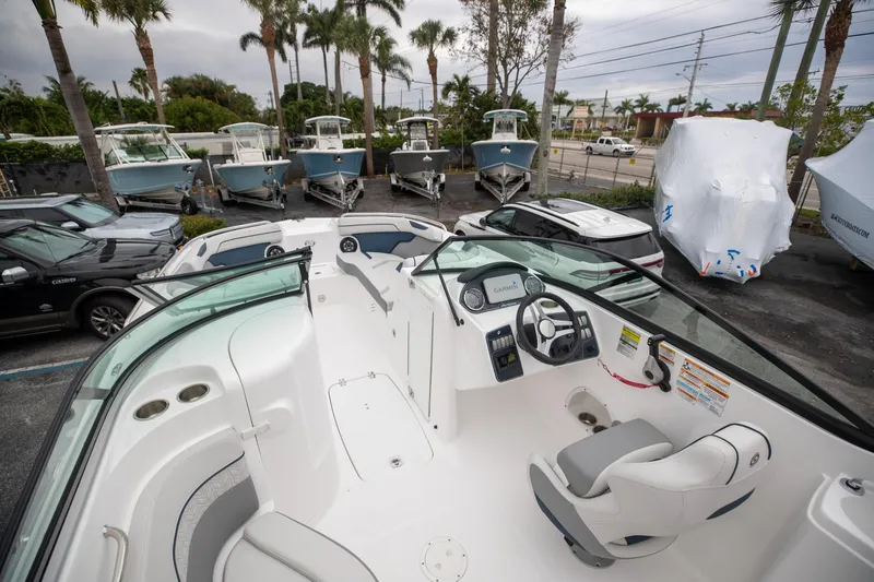 Slide: The Image of 2023 Hurricane SunDeck 2200 OB boat interior with steering console and seating, parked among other boats. - 9