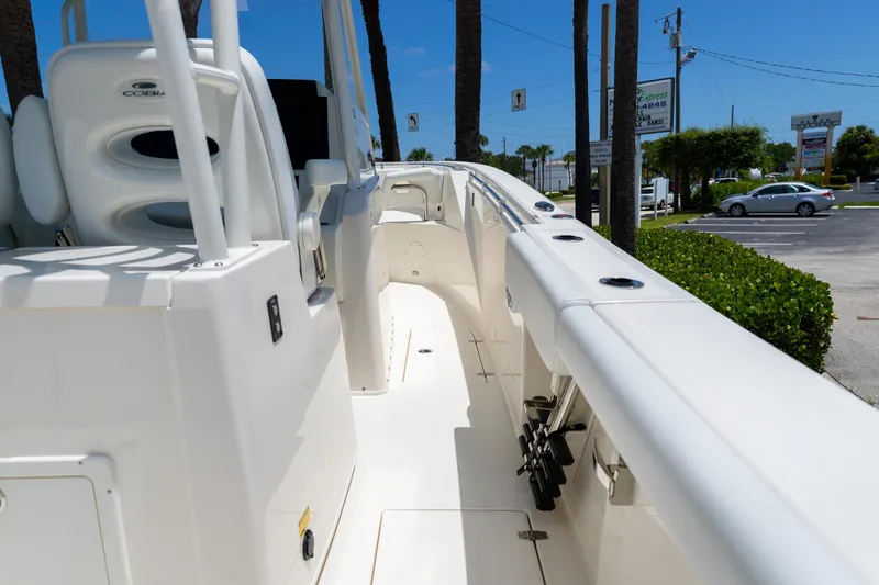 Slide: The Image of 2024 Cobia 320 CC boat interior with seating and rod holders, parked outdoors. - 14