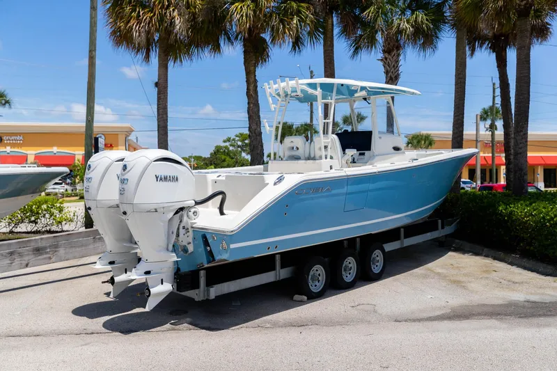Slide: The Image of 2024 Cobia 320 CC boat with twin Yamaha engines on a trailer, parked outdoors. - 2
