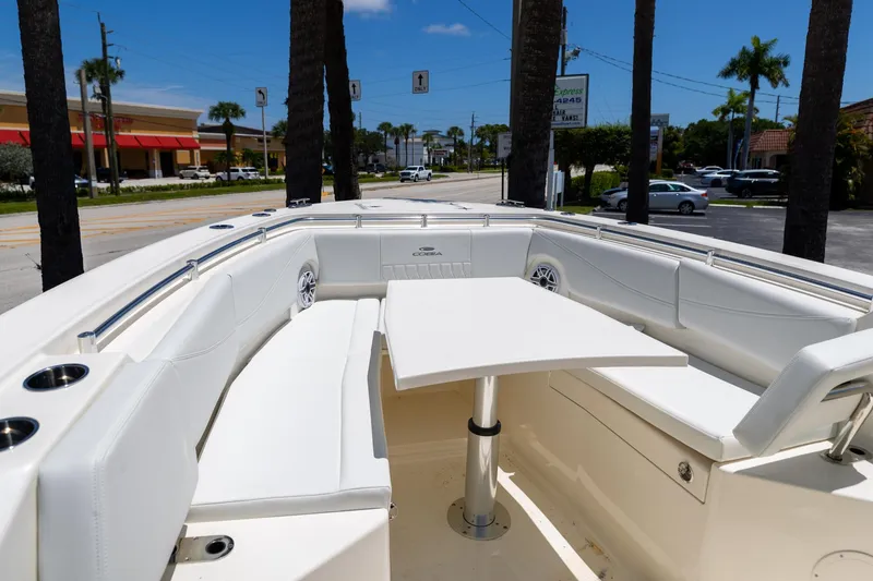 Slide: The Image of 2024 Cobia 320 CC boat interior with white seating and table, parked near palm trees. - 34