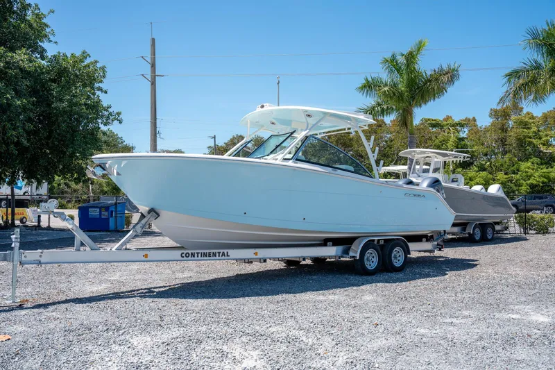 Slide: The Image of 2024 Cobia 280 DC boat on trailer, parked outdoors under clear blue sky. - 2