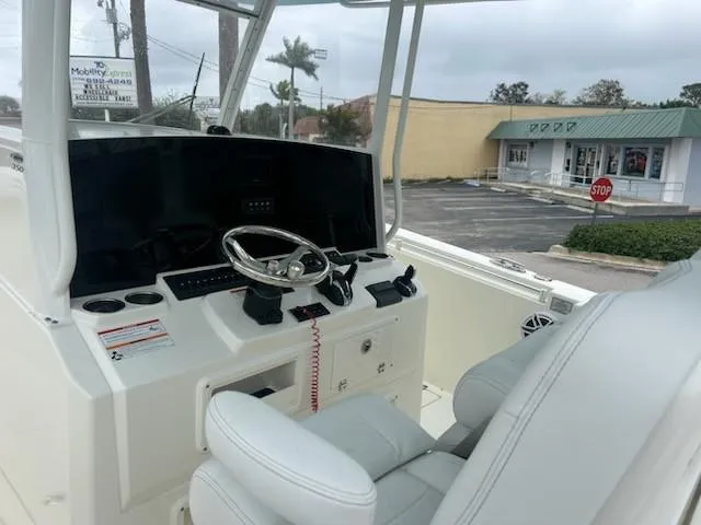 Slide: The Image of 2024 Cobia 350 CC boat cockpit with steering wheel and controls, parked near a shopping area. - 4