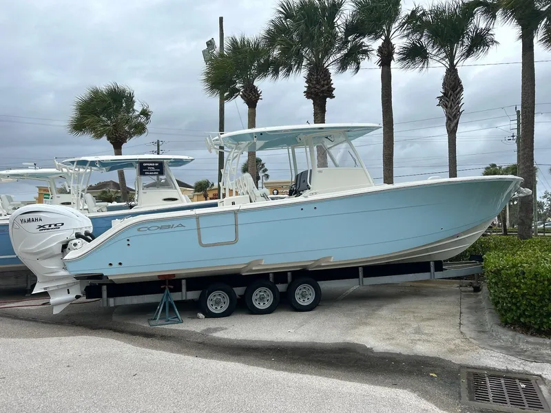 Slide: The Image of 2024 Cobia 350 CC boat on trailer with Yamaha engines, parked near palm trees. - 1