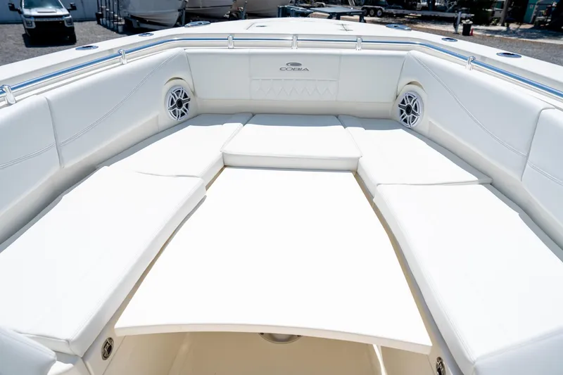 Slide: The Image of 2024 Cobia 320 CC boat interior with white cushioned seating and built-in speakers. - 45