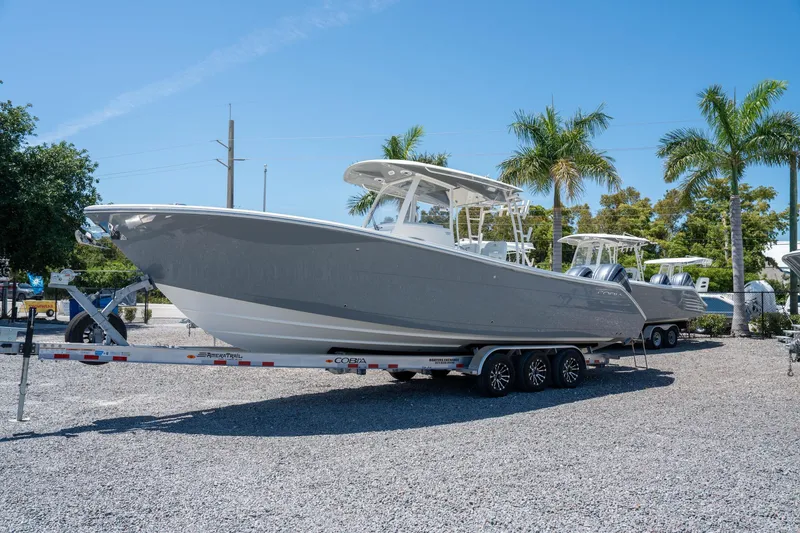 Slide: The Image of 2024 Cobia 320 CC boat on trailer, parked outdoors with palm trees in the background. - 2