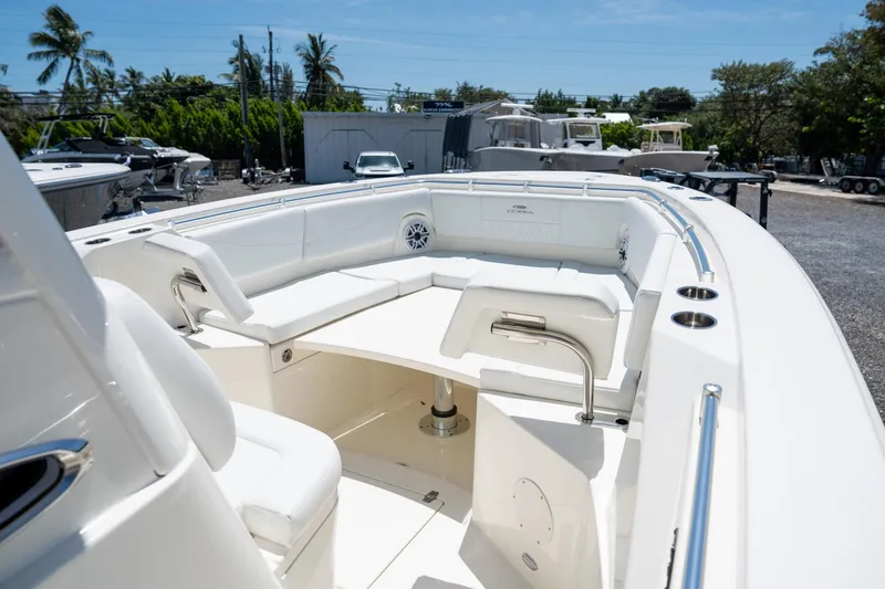 Slide: The Image of 2024 Cobia 320 CC boat interior with white seating and table, parked outdoors. - 37