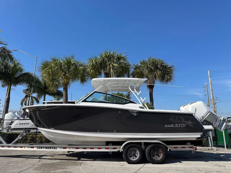 Slide: The Image of 2024 Blackfin 272DC boat on trailer, parked under palm trees, clear blue sky. - 1